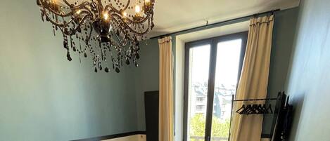 A dining area with a table set for two, a sofa, a chandelier, and a view of the outdoors.