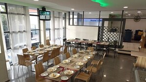 A dining area with multiple tables set for guests, a television screen, and a Hostel Center sign.