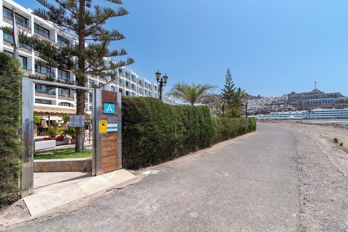 L’entrée d’un hôtel au design moderne, avec un chemin d’accès dégagé et une vue sur la mer et les bâtiments en arrière-plan.