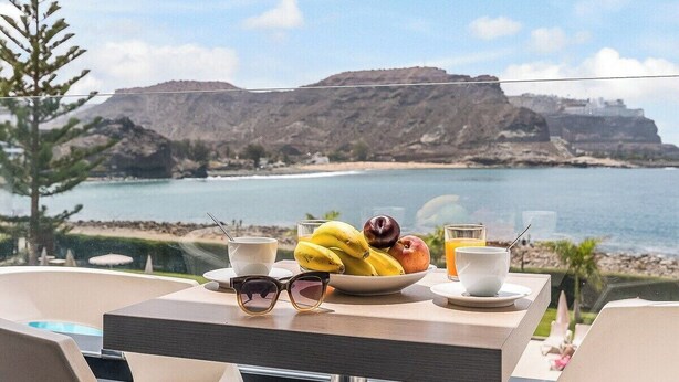 Une table dressée avec des aliments pour le petit-déjeuner, offrant une vue panoramique sur un paysage côtier.