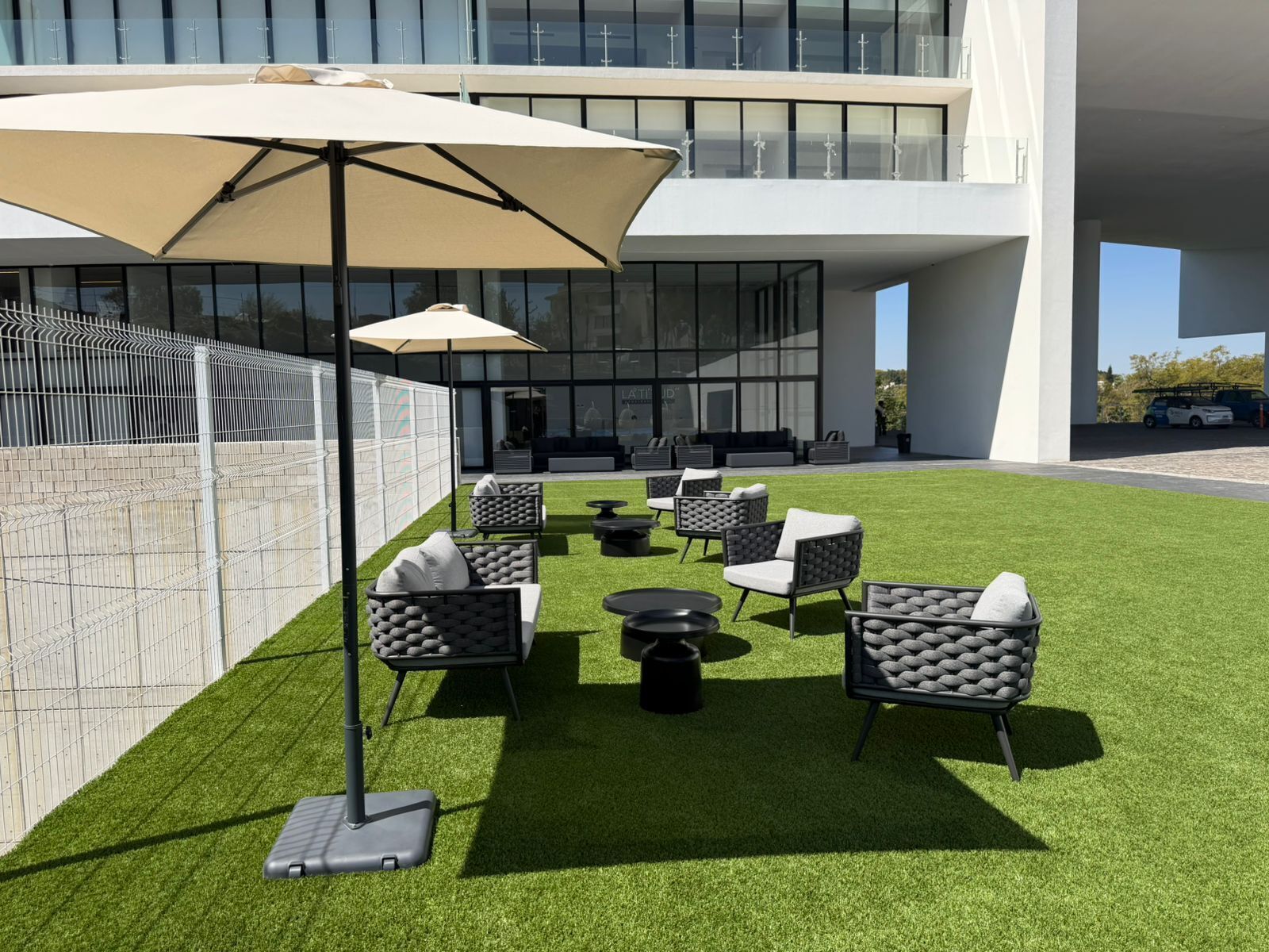 Un área de estar al aire libre con césped artificial, sillas modernas, una mesa y un paraguas grande.