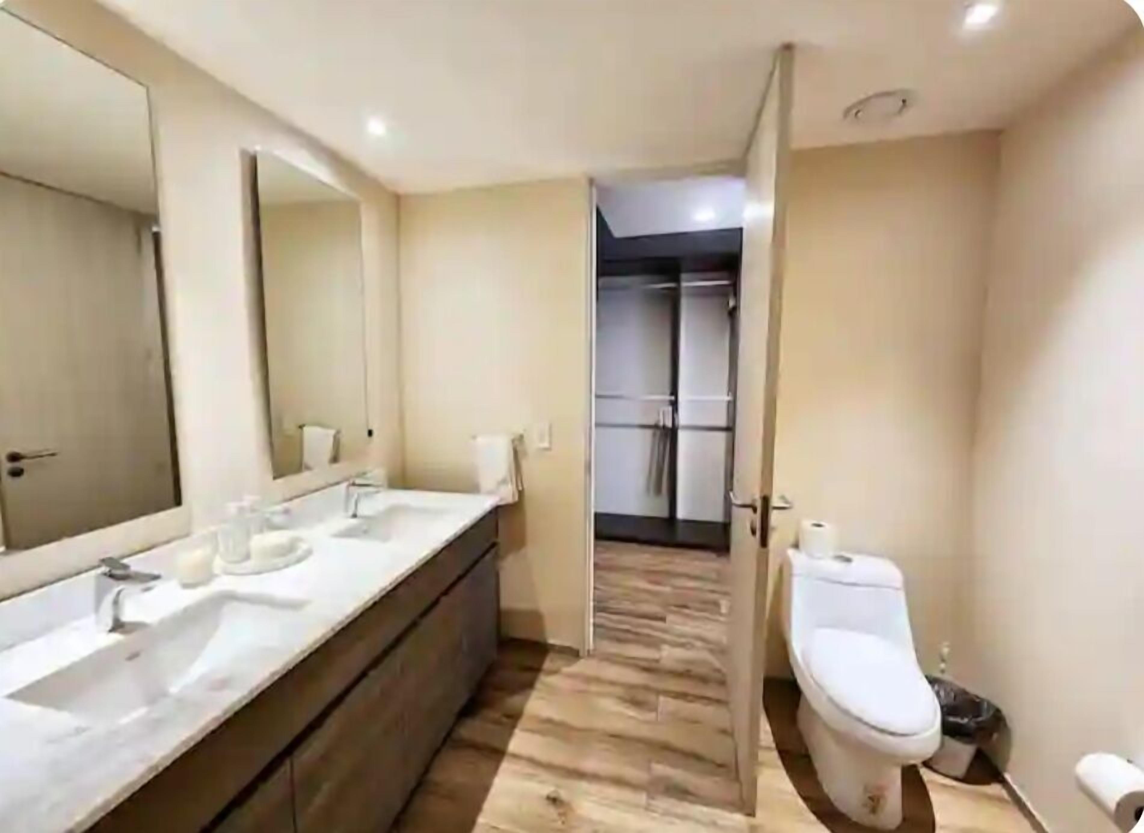 Ein modernes Badezimmer mit einem großen Spiegel, zwei Waschbecken, einer Toilette und einer Duschkabine.