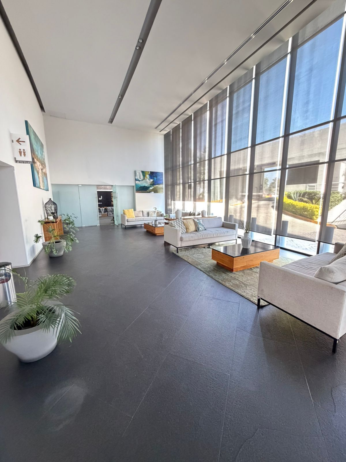 Ein geräumiger, moderner Lounge-Bereich mit großen Fenstern, einer Sofagarnitur und Topfpflanzen.