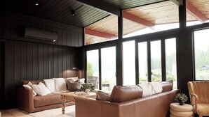 Ein modernes Wohnzimmer mit zwei braunen Ledersofas, einem Holztisch und einem runden Beistelltisch mit Pflanze. Große Fenster sorgen für natürliches Licht und einen Blick ins Freie.