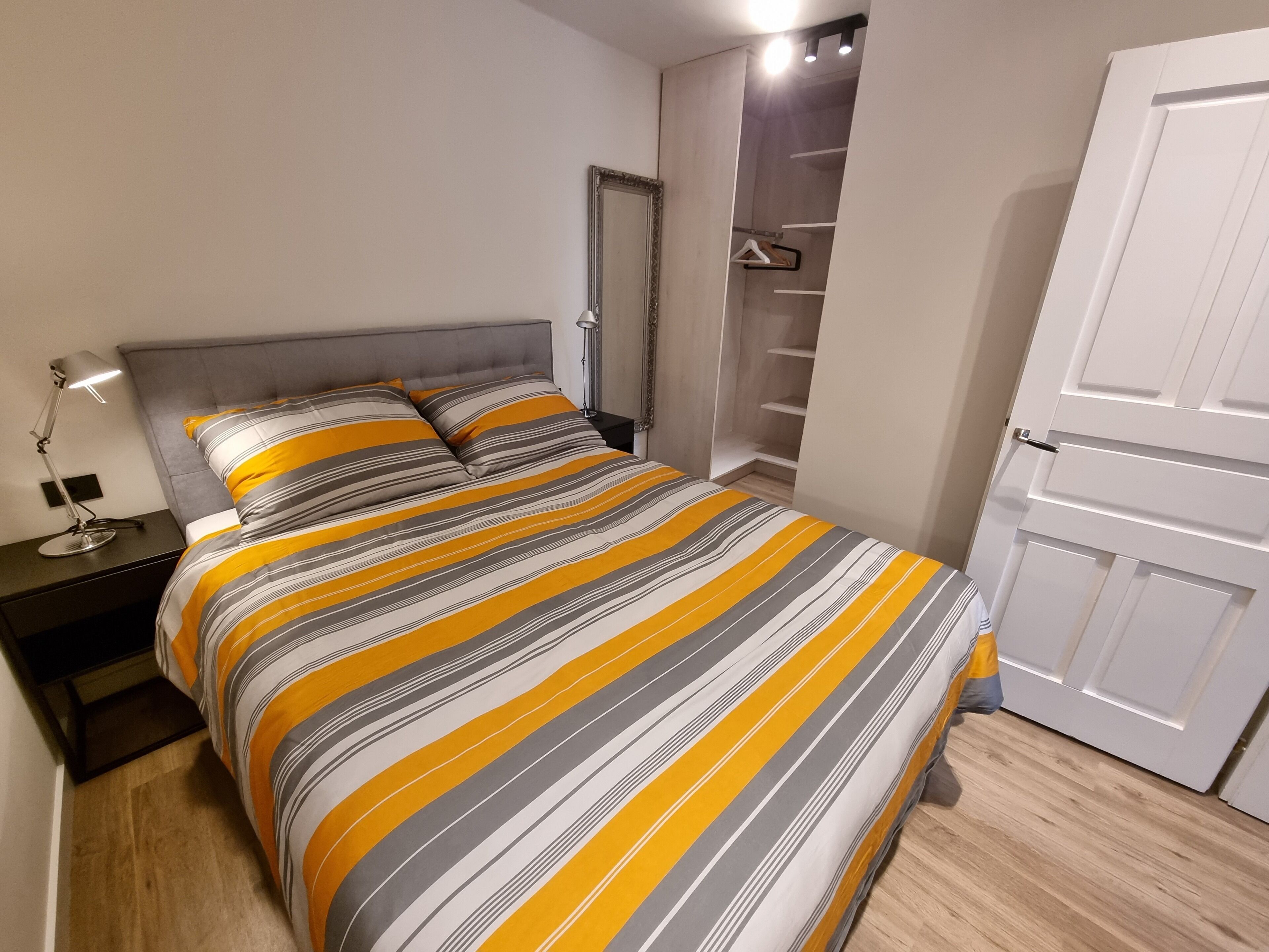 Une chambre à coucher comprenant un lit, une table de chevet, une lampe de chevet, une armoire et une porte.