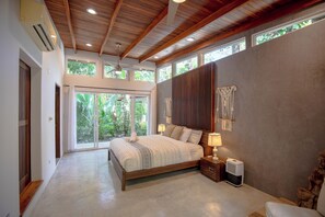 A bedroom with a large bed, wooden ceiling, and a view of greenery through the windows. - Lovely Villa with private path to Surf in Guiones (Nosara)