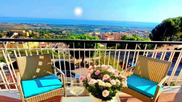 Un balcon avec des fauteuils en osier, une table et un pot de fleurs.