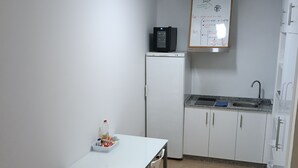 A small kitchenette with a refrigerator, microwave, and sink. There is a whiteboard with notes above the sink. A table with chairs is in the foreground. - Large renovated country house in a relaxing natural location (Pontevedra)