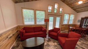 Une pièce spacieuse avec un plafond en bois, un ensemble de canapés rouges, une table basse noire et un coin repas comprenant des chaises et une table en bois.