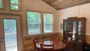 Un coin repas avec une table et des chaises en bois, un meuble avec des portes en verre et des fenêtres équipées de stores.