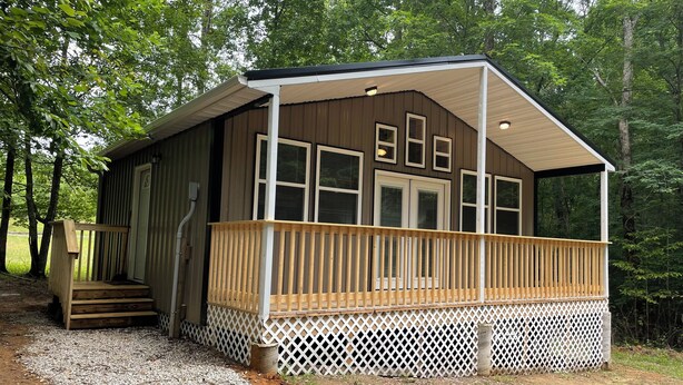 Une cabane dotée d’une terrasse en bois, d’un porche couvert et d’une allée gravillonnée.