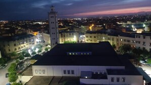 Un paisaje urbano al atardecer con un edificio blanco destacado que cuenta con una torre, rodeado de otras edificaciones residenciales y comerciales.