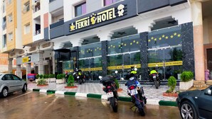 Un hotel con un letrero llamativo, varias motocicletas estacionadas frente a él, y el suelo mojado que indica lluvia reciente.