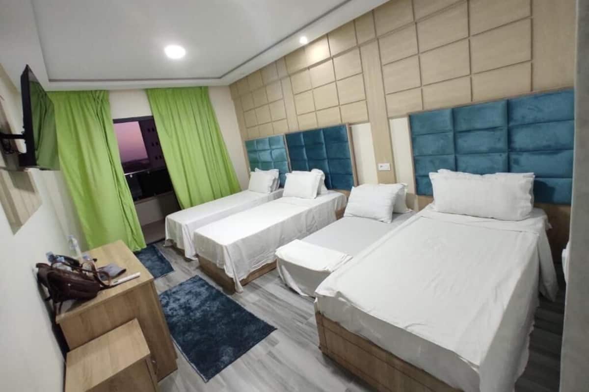 A hotel room with three beds, a desk, and a TV.