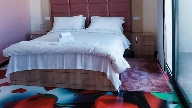 Una habitación de hotel con cama, mesita de noche, ventana y una alfombra colorida.