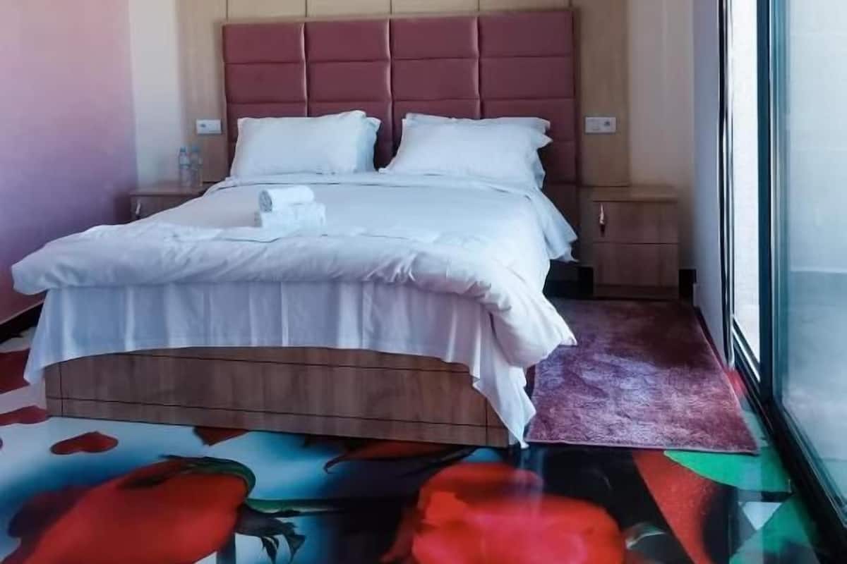 A hotel room with a bed, a nightstand, a window, and a colorful carpet.