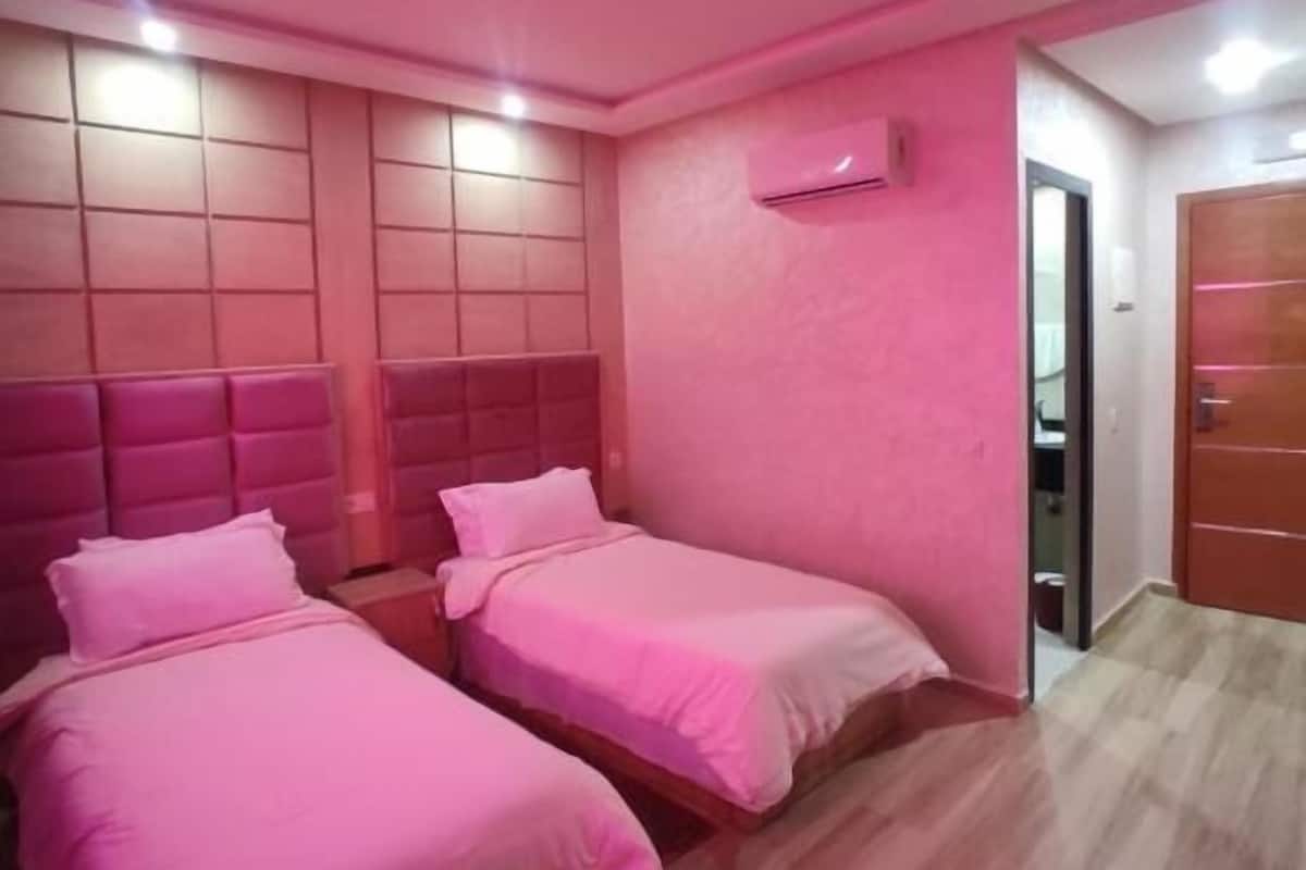 A room with two beds, a wooden floor, and a pink color scheme.