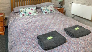 Siististi pedattu sänky, jossa on kukkakuosiset vuodevaatteet, kaksi tyynyä ja kaksi taitetusti sängylle asetettua pyyhettä.