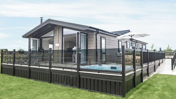 A modern house with a glass-enclosed deck, a hot tub, and a covered patio area.