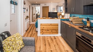 A modern kitchen with wooden cabinets, a central island, and a dining area with a grey sofa. - 4 bedroom accommodation in Eoropie, Isle of Lewis (Eoropie, Isle of Lewis)