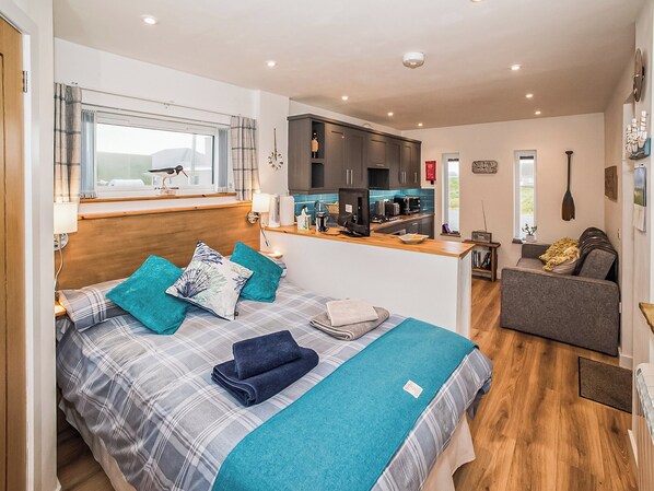 A compact bedroom with a bed, a small kitchenette, and a seating area.