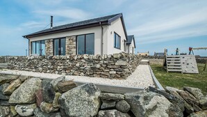 A modern house with large windows, a stone wall, and a wooden deck. - 4 bedroom accommodation in Eoropie, Isle of Lewis (Eoropie, Isle of Lewis)