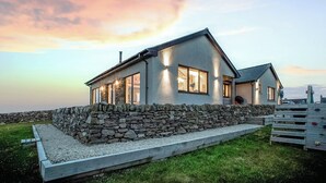 A modern house with a stone wall foundation, large windows, and a well-maintained lawn. - 4 bedroom accommodation in Eoropie, Isle of Lewis (Eoropie, Isle of Lewis)