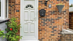 A white door with a number plate, a mailbox, and a hanging light fixture on a brick wall. - 1 bedroom accommodation in Glossop (Glossop)