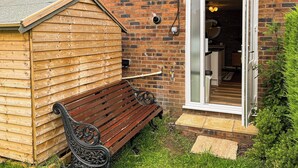 A wooden shed with a bench, a brick wall, and a door leading to a room with a fireplace. - 1 bedroom accommodation in Glossop (Glossop)