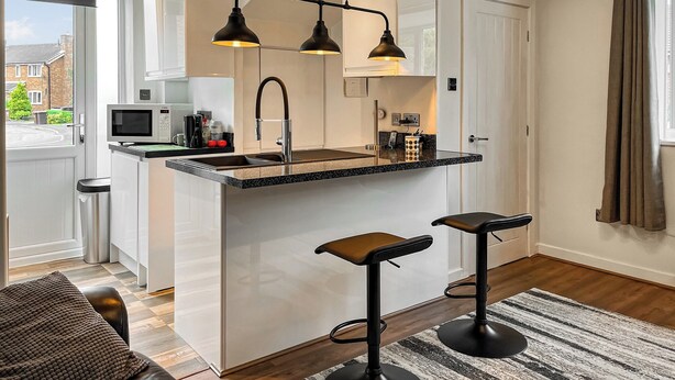 A modern kitchen with a central island, two bar stools, and pendant lighting. - 1 bedroom accommodation in Glossop (Glossop)