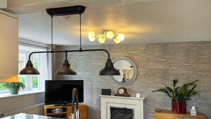 A modern kitchen with a built-in stove, a large island with a sink, and a flat-screen TV. - 1 bedroom accommodation in Glossop (Glossop)