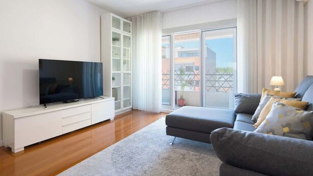 Ein modernes Wohnzimmer mit Flachbildfernseher, grauem Sofa und einer weißen Unterhaltungseinheit.