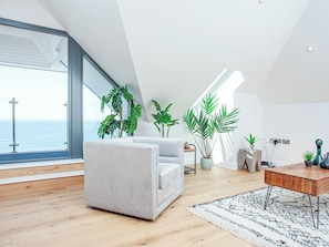 A modern living room with a large window, a sofa, a coffee table, and several potted plants.