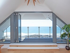 A modern interior with a large glass door leading to a balcony overlooking the ocean.