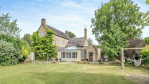 A stone house with a conservatory, a hammock, and a well-maintained lawn.