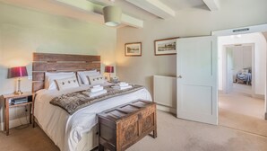 A bedroom with a wooden headboard, a bedside table with a lamp, a radiator, and a door leading to another room.