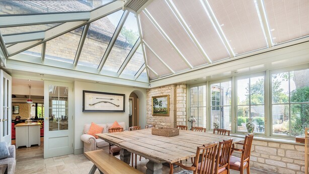 A spacious room with a large wooden table, comfortable seating, and a glass ceiling allowing natural light.