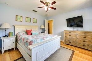 Une chambre à coucher comprenant un lit, des tables de chevet, une commode, un ventilateur de plafond et un téléviseur.