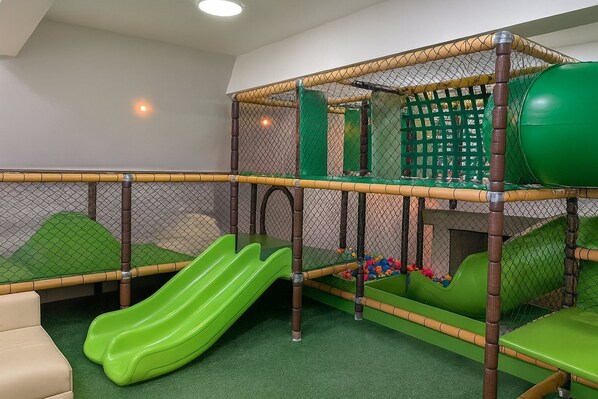 Zona de juegos infantiles con tobogán, red de escalada y asientos acolchados.