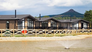 A row of modern cabins with large windows, a wooden fence, and a mountain in the background. - River Tees Lodge - UKC4064 (Great Ayton, near Stokesley)