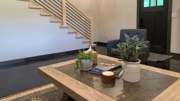 Un salon moderne avec un escalier, une porte sombre, un fauteuil gris et une table basse agrémentée d’objets décoratifs.