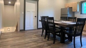Un coin repas avec une table et des chaises en bois, une porte blanche et une cuisine équipée d’armoires et d’appareils électroménagers.