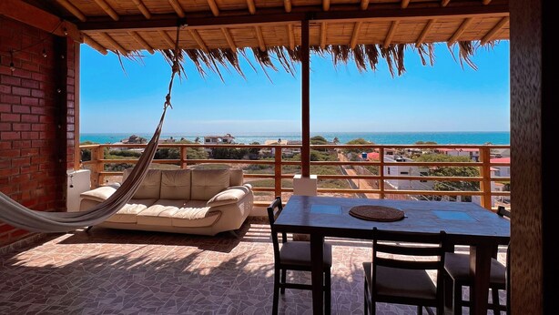 A covered outdoor seating area with a table and chairs, a hammock, and a view of the ocean. - Gamora Hotel Playa (Los Organos)