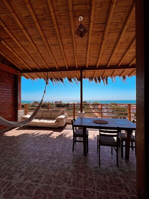 Ein überdachter Außenbereich mit Tisch und Stühlen, einer Hängematte und Blick auf das Meer.