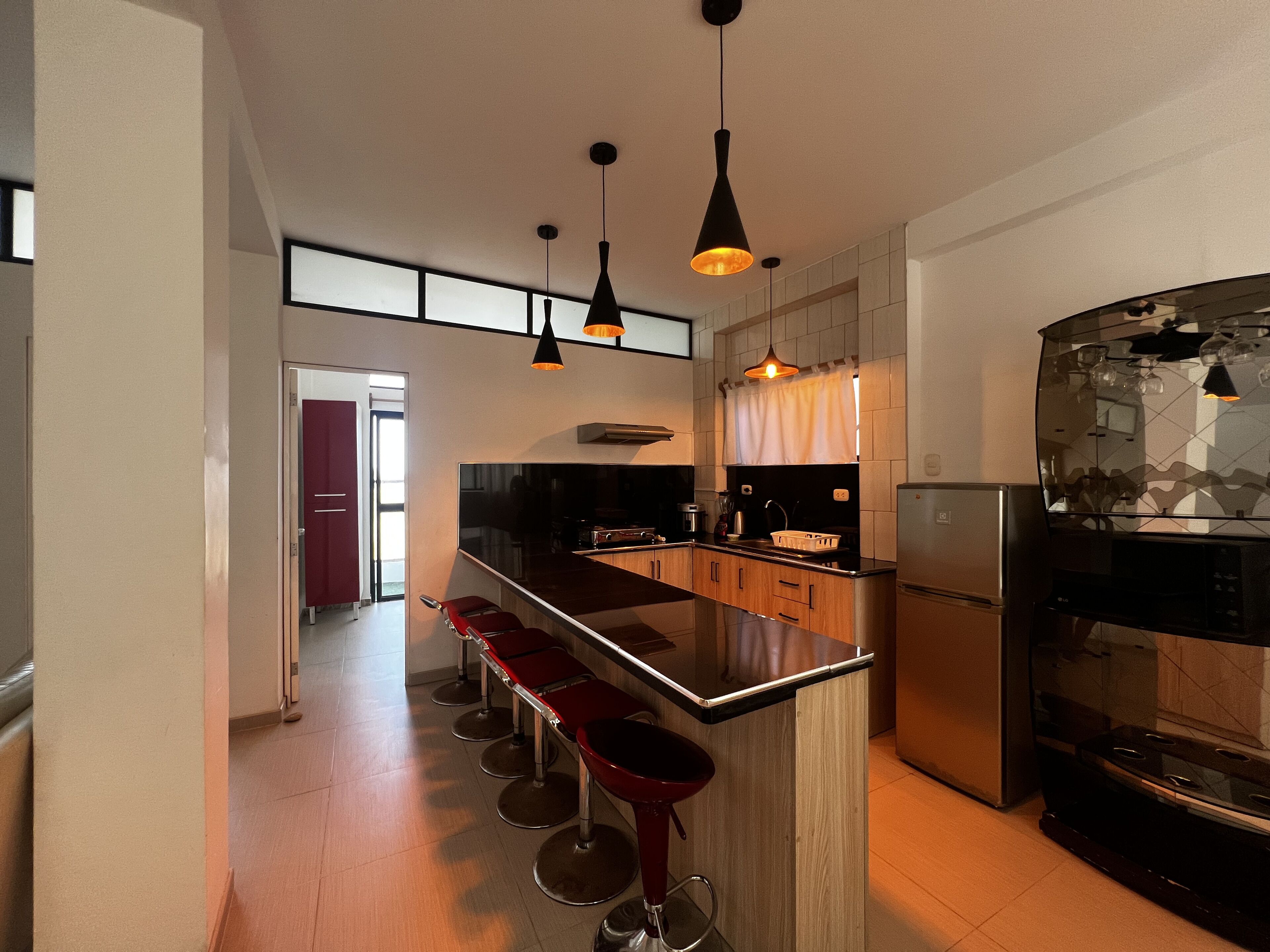 A modern kitchen with a central island, bar stools, a refrigerator, and pendant lighting.