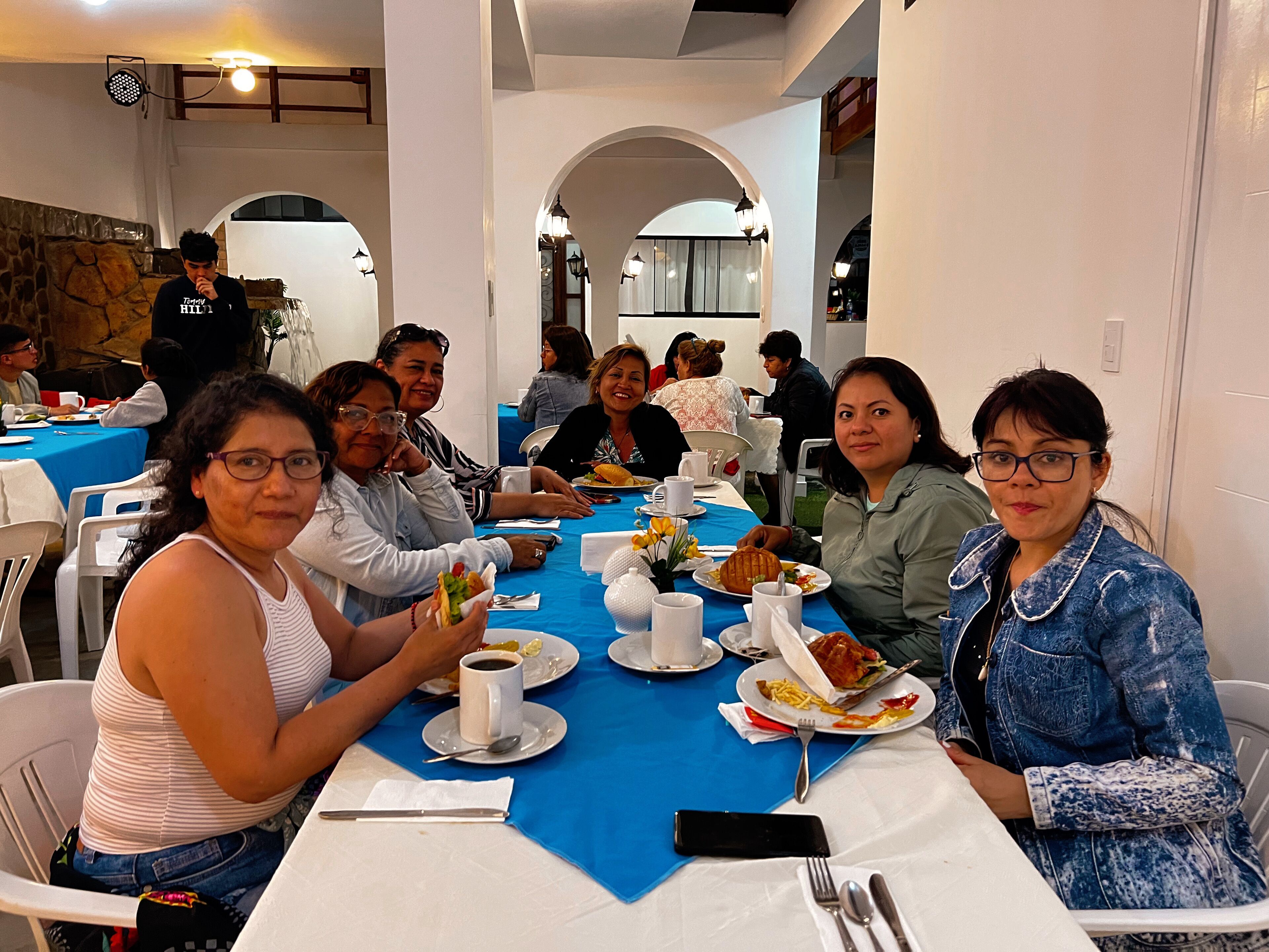 A group of people seated at a table with a blue tablecloth, white plates, and cups.