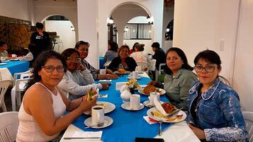 A group of people seated at a table with a blue tablecloth, white plates, and cups.