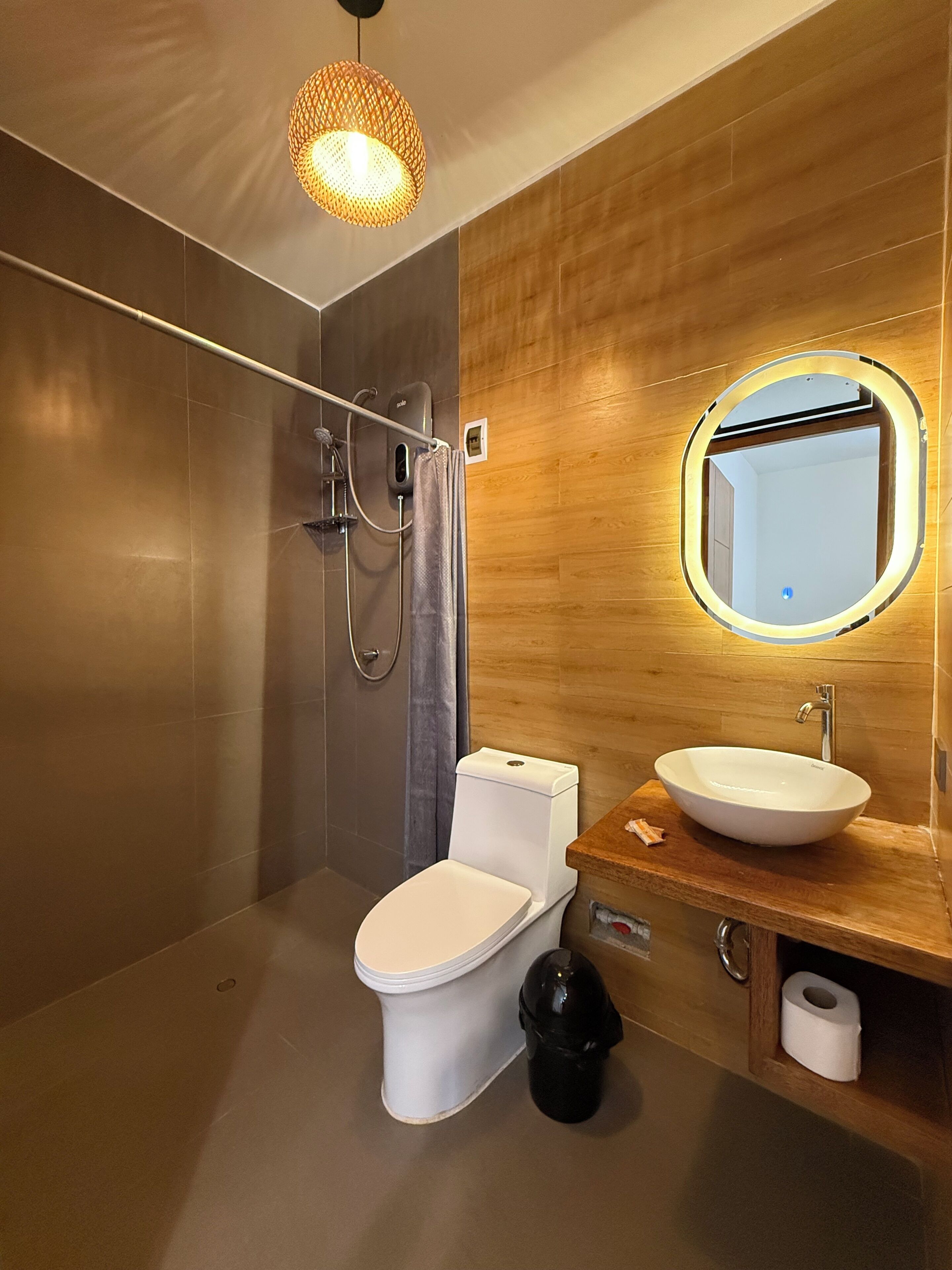 A modern bathroom with a toilet, bidet, and sink, wooden wall paneling, and a hanging light fixture.