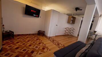 Una sala de estar moderna con piso de madera estampado, un televisor montado mostrando Netflix, un ventilador de techo y un sofá.