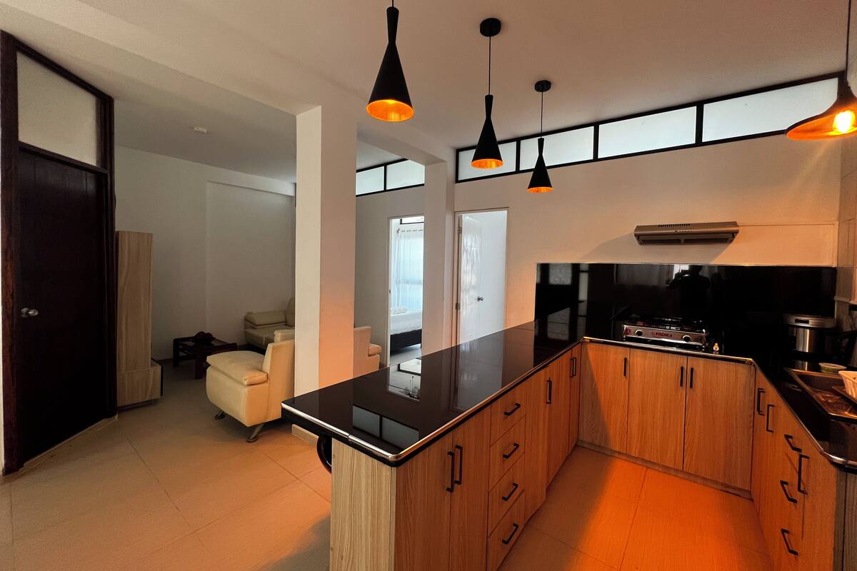 Una cucina moderna con isola centrale, lampade a sospensione nere e mobili in legno.